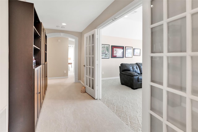 hallway with arched walkways, recessed lighting, light carpet, baseboards, and french doors