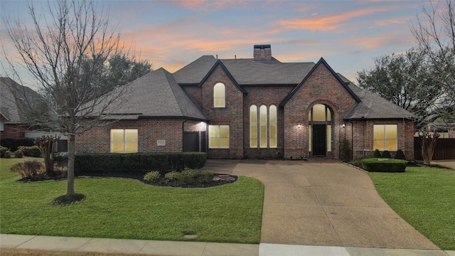 view of front of property featuring driveway, a front yard, a chimney, and brick siding