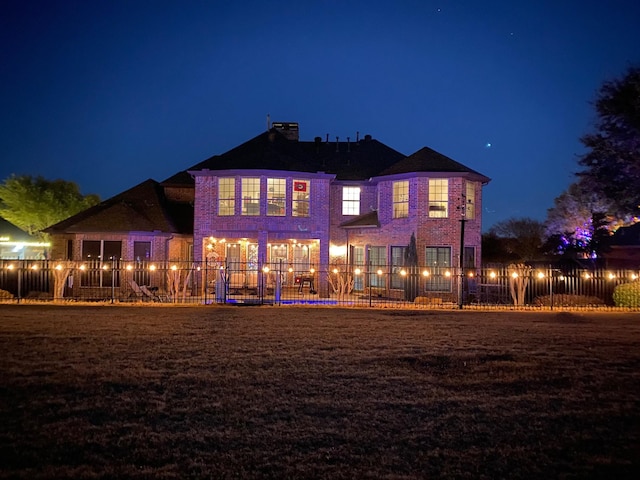 back of house at night with brick siding, a chimney, and fence