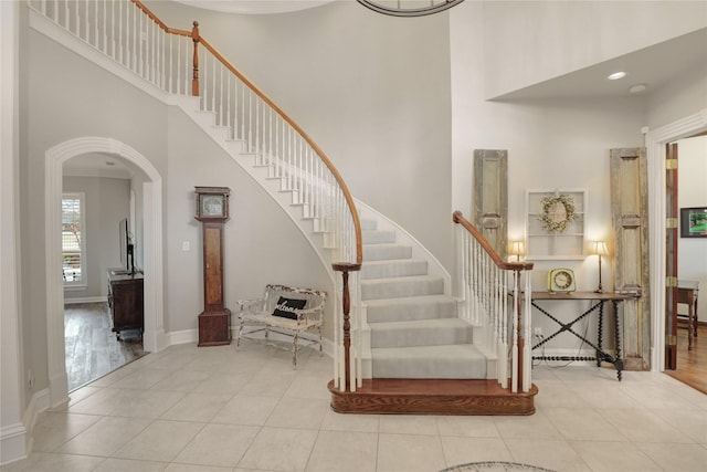 staircase with arched walkways, a high ceiling, tile patterned flooring, and baseboards