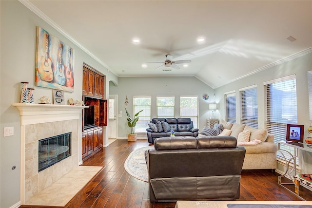 living area featuring dark wood-type flooring, a ceiling fan, baseboards, a tiled fireplace, and crown molding