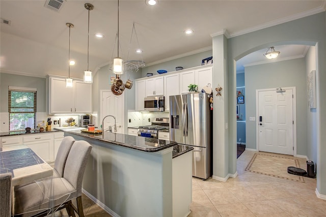 kitchen featuring pendant lighting, visible vents, appliances with stainless steel finishes, a kitchen island with sink, and white cabinets