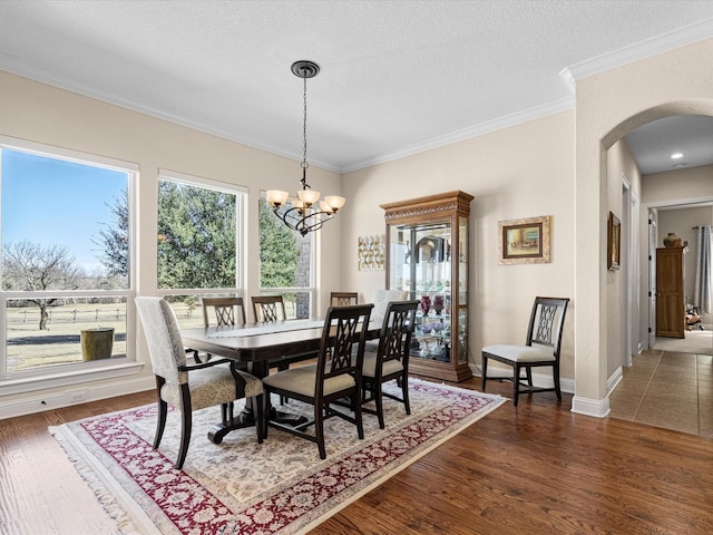 dining room with arched walkways, crown molding, dark wood finished floors, and a chandelier