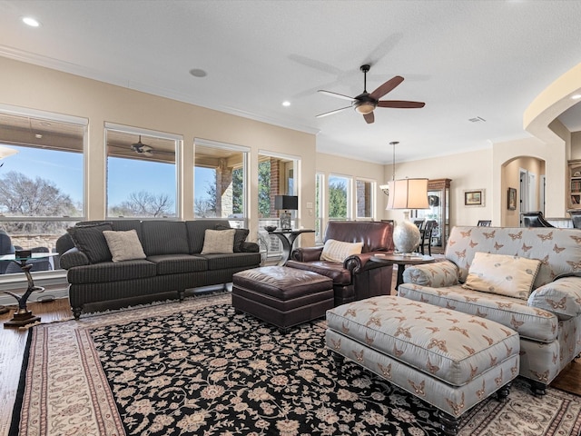 living room featuring arched walkways, ceiling fan, wood finished floors, and crown molding