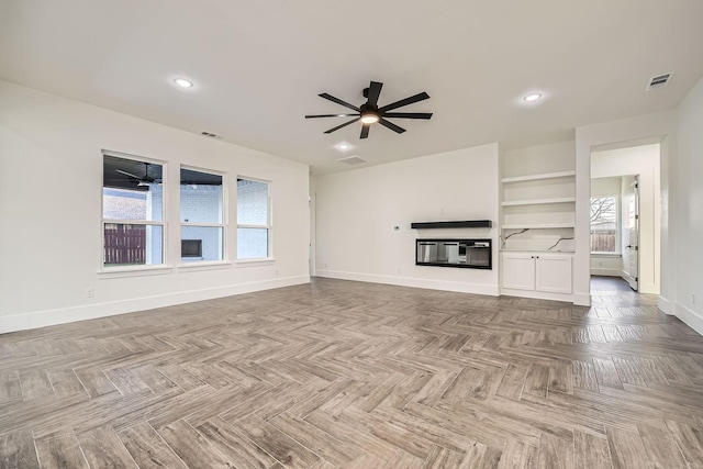 unfurnished living room with plenty of natural light, baseboards, visible vents, and a glass covered fireplace