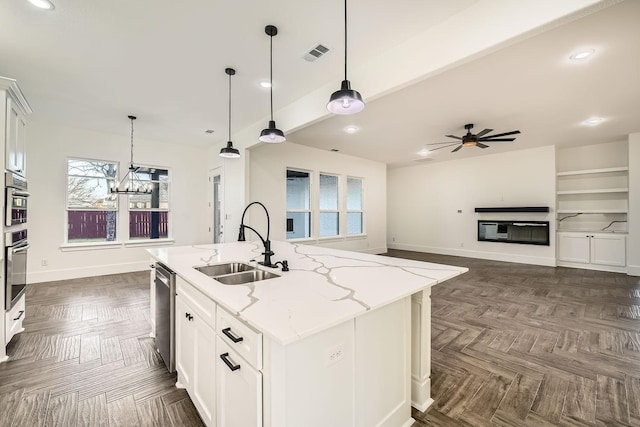 kitchen featuring visible vents, white cabinets, an island with sink, light stone counters, and a sink