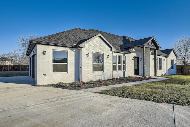 view of front of house featuring a shingled roof, a front yard, brick siding, and fence