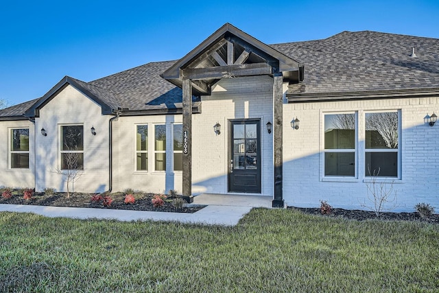 view of front of house with roof with shingles, a front yard, and brick siding