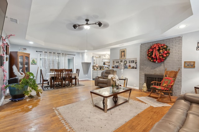 living room with recessed lighting, a raised ceiling, visible vents, a brick fireplace, and wood finished floors