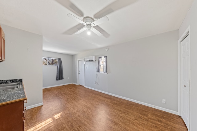 interior space featuring a sink, wood finished floors, a ceiling fan, baseboards, and a wall mounted air conditioner