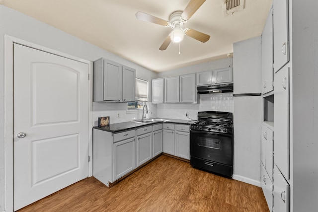 kitchen featuring dark countertops, gray cabinets, black range with gas stovetop, a sink, and under cabinet range hood