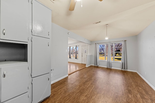 interior space with dark wood-type flooring, visible vents, baseboards, vaulted ceiling, and a ceiling fan