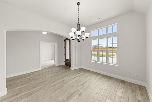 empty room with an inviting chandelier, light wood finished floors, arched walkways, baseboards, and visible vents
