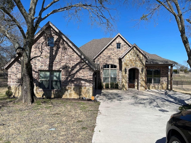 french country style house with stone siding, brick siding, driveway, and roof with shingles