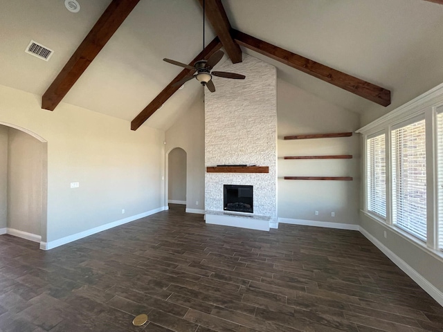 unfurnished living room featuring baseboards, visible vents, arched walkways, dark wood-style flooring, and a stone fireplace