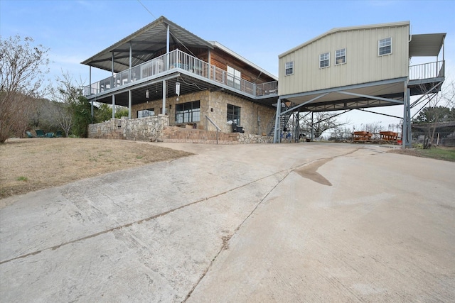 rear view of house featuring a balcony, stone siding, and driveway