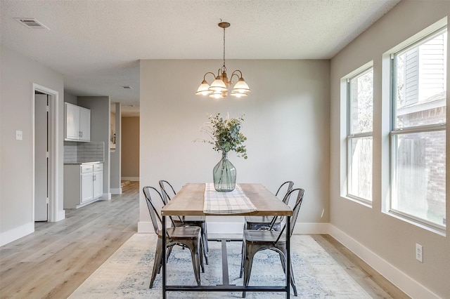 dining area featuring a chandelier, a textured ceiling, and light wood-type flooring