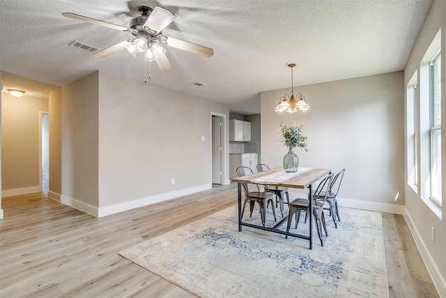 dining space with light wood-style floors, baseboards, visible vents, and a textured ceiling