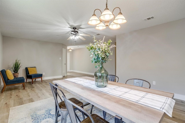 dining space featuring light wood finished floors, baseboards, visible vents, and ceiling fan with notable chandelier