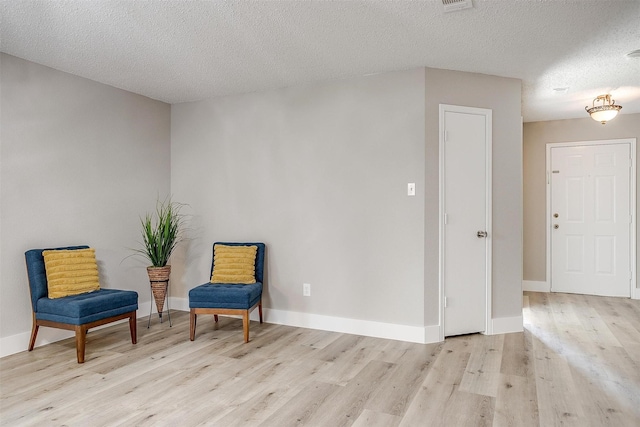 living area with light wood-style flooring, baseboards, and a textured ceiling