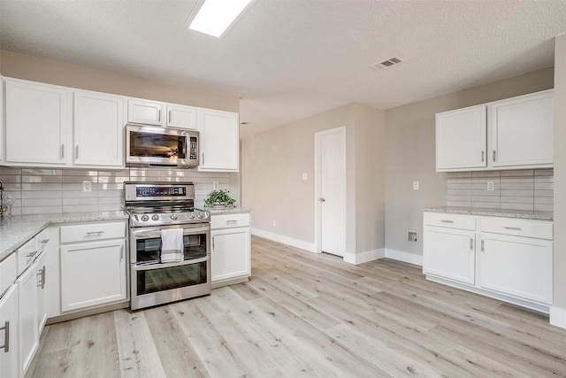 kitchen featuring light wood-type flooring, light stone countertops, appliances with stainless steel finishes, and white cabinets