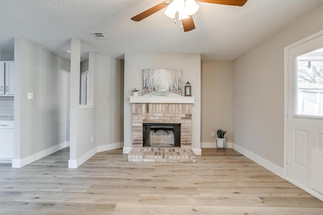 unfurnished living room featuring baseboards, visible vents, a textured ceiling, light wood-type flooring, and a brick fireplace