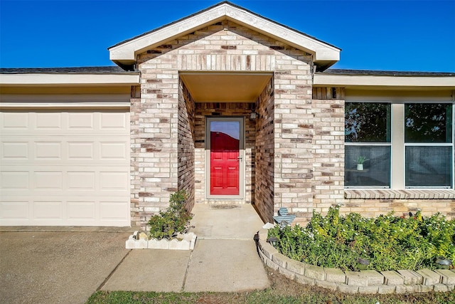 view of exterior entry featuring a garage and brick siding