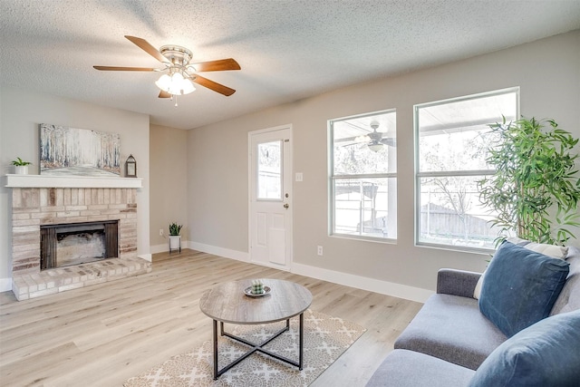 living room featuring a textured ceiling, ceiling fan, baseboards, light wood-style floors, and a brick fireplace