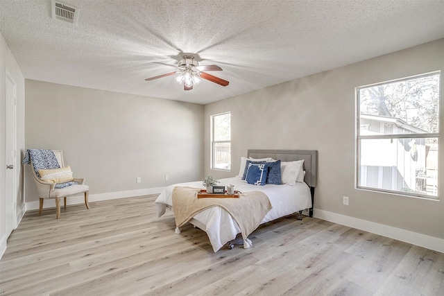 bedroom with baseboards, light wood-style flooring, visible vents, and a textured ceiling