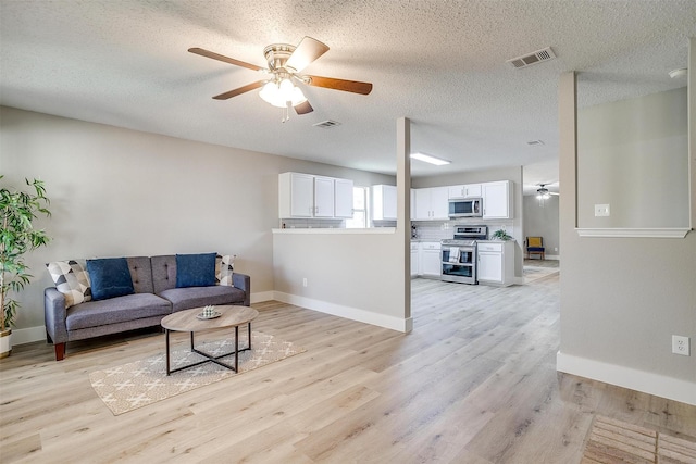 living room featuring visible vents, light wood-type flooring, a ceiling fan, and baseboards