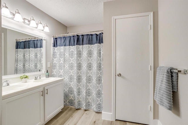 full bath with double vanity, a textured ceiling, a sink, and wood finished floors