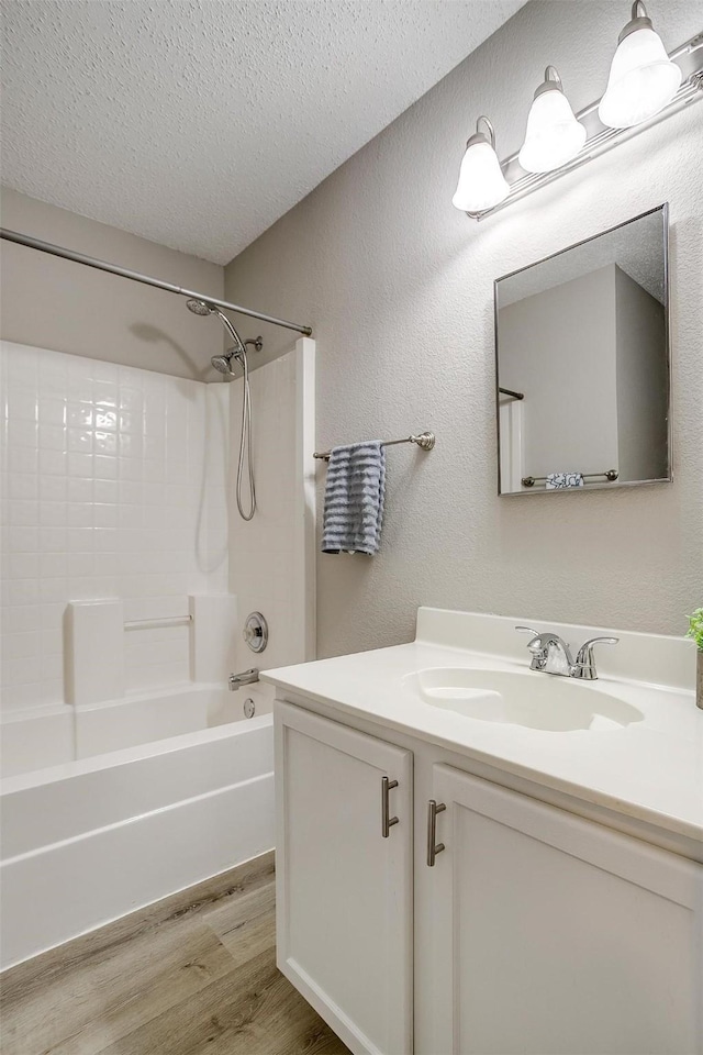 full bathroom with a textured ceiling, a textured wall, wood finished floors, vanity, and shower / washtub combination