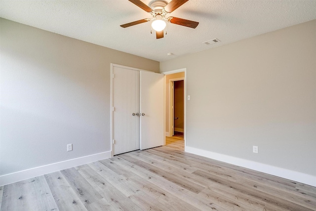 spare room featuring visible vents, light wood-style floors, ceiling fan, a textured ceiling, and baseboards