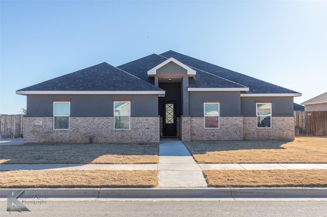 view of front facade with a shingled roof, fence, and stucco siding