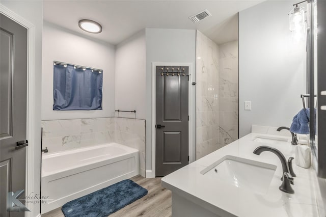 full bathroom featuring double vanity, visible vents, a sink, wood finished floors, and a bath