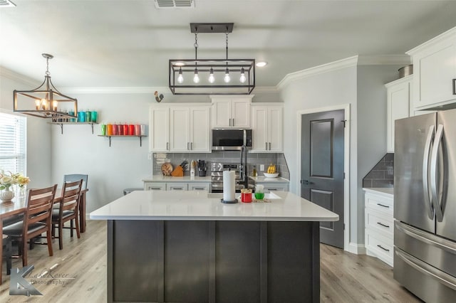 kitchen with white cabinets, a kitchen island, appliances with stainless steel finishes, decorative light fixtures, and light countertops