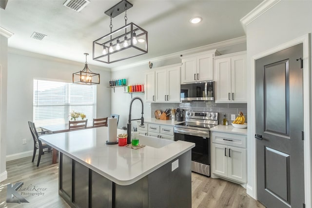 kitchen featuring hanging light fixtures, appliances with stainless steel finishes, white cabinets, and an island with sink