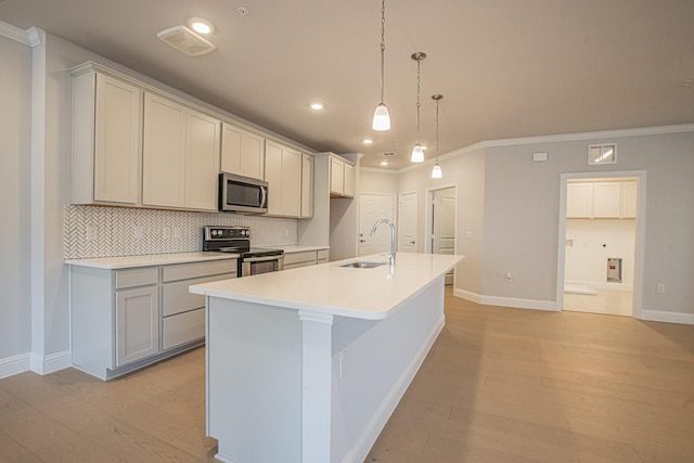 kitchen featuring light wood-style flooring, light countertops, appliances with stainless steel finishes, hanging light fixtures, and an island with sink