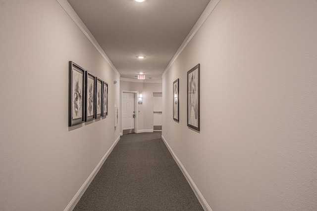 hallway featuring ornamental molding, dark colored carpet, and baseboards