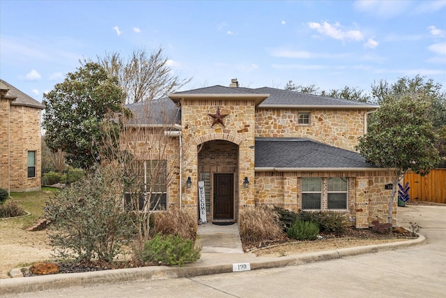 french country style house featuring stone siding, a shingled roof, and fence