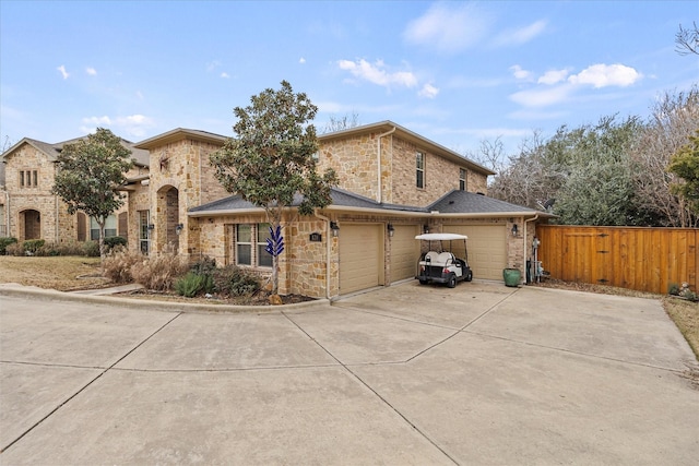 view of front of house with driveway, stone siding, an attached garage, and fence