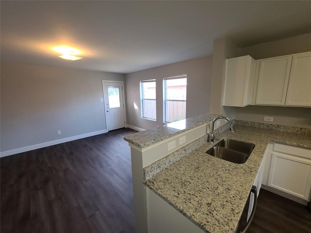 kitchen with light stone counters, white cabinets, a sink, a peninsula, and baseboards