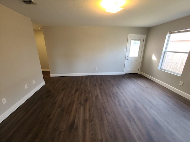 empty room with visible vents, baseboards, and dark wood finished floors