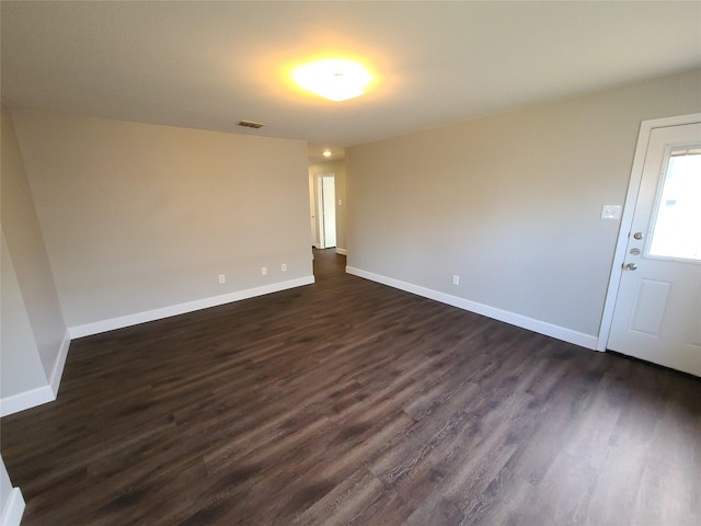 unfurnished room with dark wood-style flooring, visible vents, and baseboards