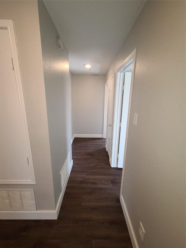 hallway with baseboards, visible vents, and dark wood-style flooring