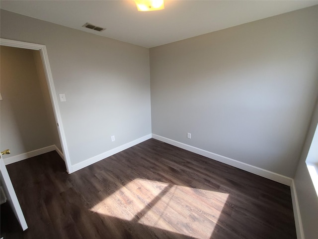 spare room with dark wood-style floors, visible vents, and baseboards