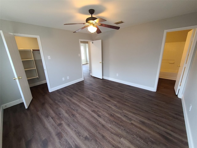 unfurnished bedroom featuring dark wood-type flooring, a ceiling fan, visible vents, baseboards, and a walk in closet