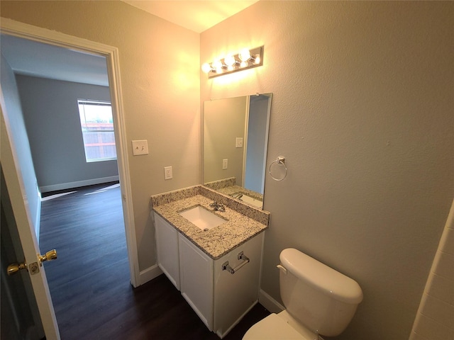 half bathroom with baseboards, vanity, toilet, and wood finished floors