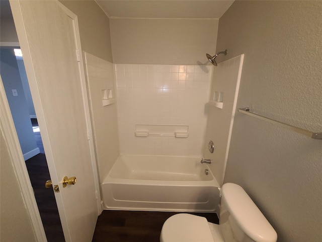 bathroom with toilet,  shower combination, wood finished floors, and a textured wall