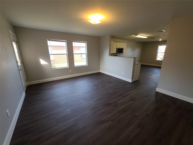 unfurnished living room with dark wood-type flooring and baseboards